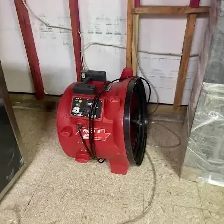 A red air mover drying a room with an opened wall and plastic sheeting