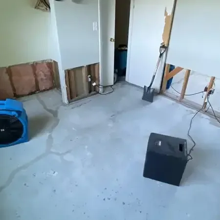 Air movers and a dehumidifier drying a room with the lower drywall cut away