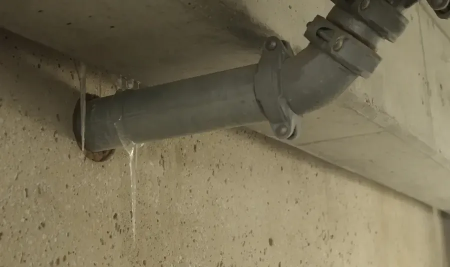 Water dripping from a cracked fitting on a pipe along a concrete wall after a hard freeze