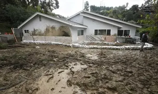Muddy storm runoff across the yard of a sandbagged house below a hillside