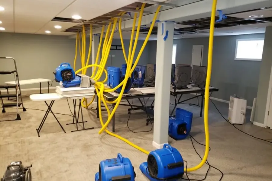 Air movers and ceiling drying hoses running in a lower-level room with ceiling panels opened